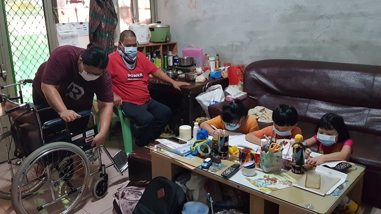 阿霞(左1)攙扶中風的先生阿華(左2)坐輪椅,3個讀小學的子女在旁寫功課。韓旭爾攝 阿霞(左1)攙扶中風的先生阿華(左2)坐輪椅,3個讀小學的子女在旁寫功課。韓旭爾攝