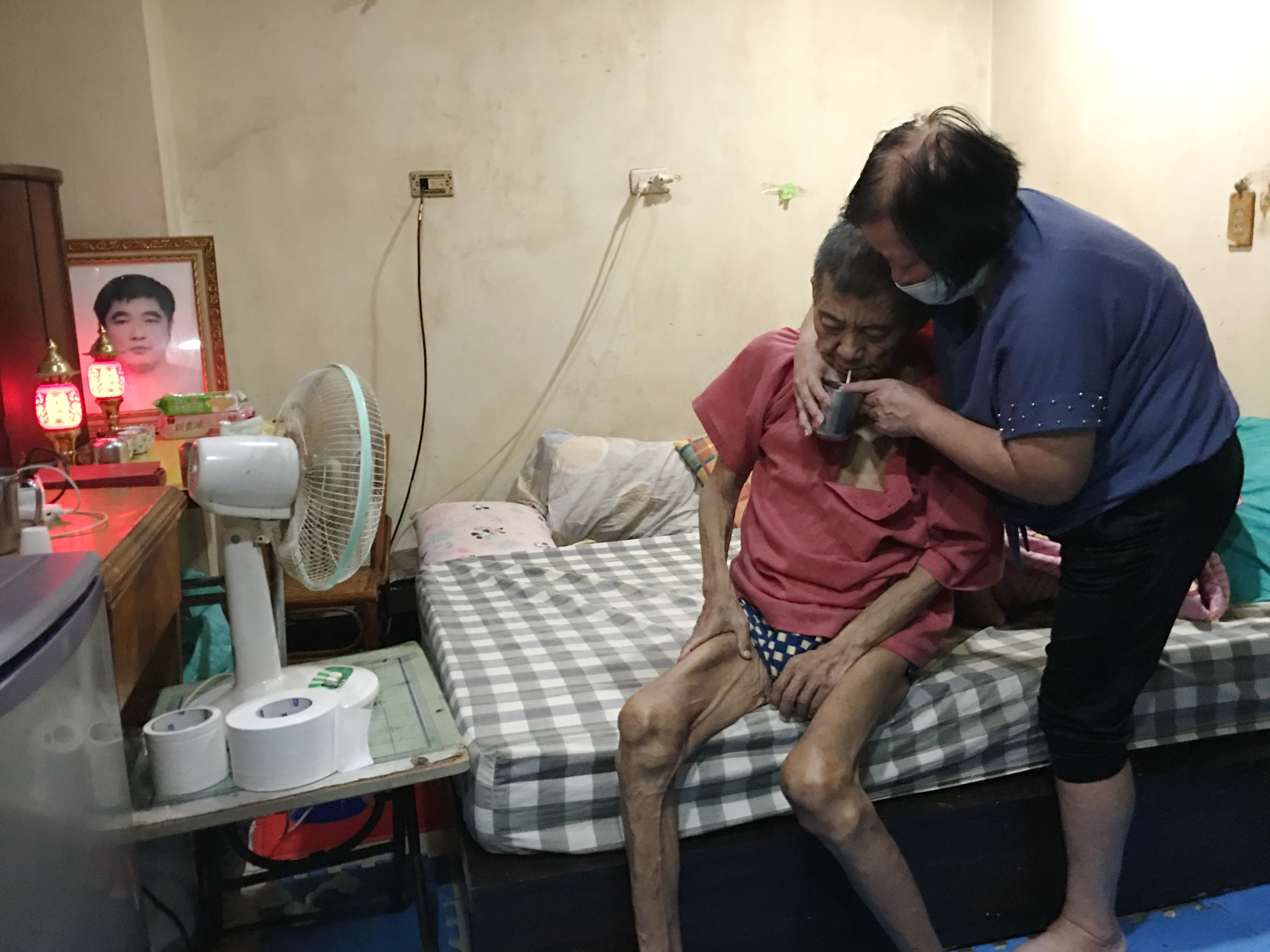 阿雄癱臥乏力,老母徐許美月(右)撐扶他起身喝水。向高彬攝 阿雄癱臥乏力,老母徐許美月(右)撐扶他起身喝水。向高彬攝