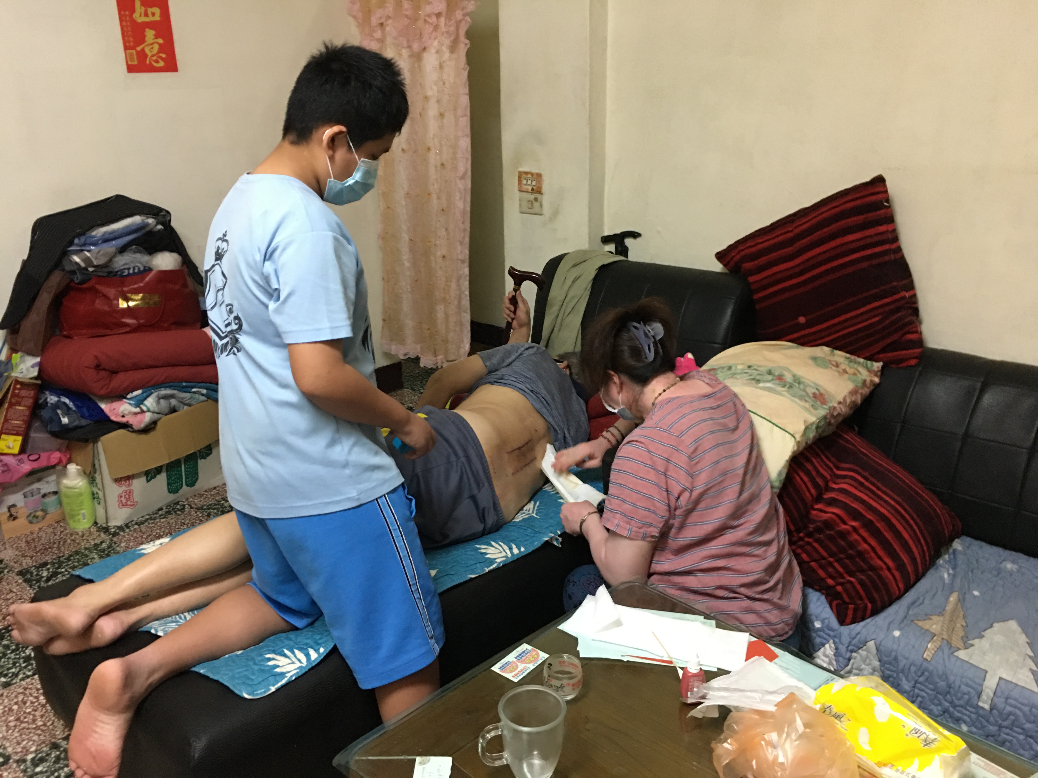 鄭燕惠(右)幫動腰椎手術後的先生清傷口、換紗布。旁為兒子小嘉。向高彬攝 鄭燕惠(右)幫動腰椎手術後的先生清傷口、換紗布。旁為兒子小嘉。向高彬攝