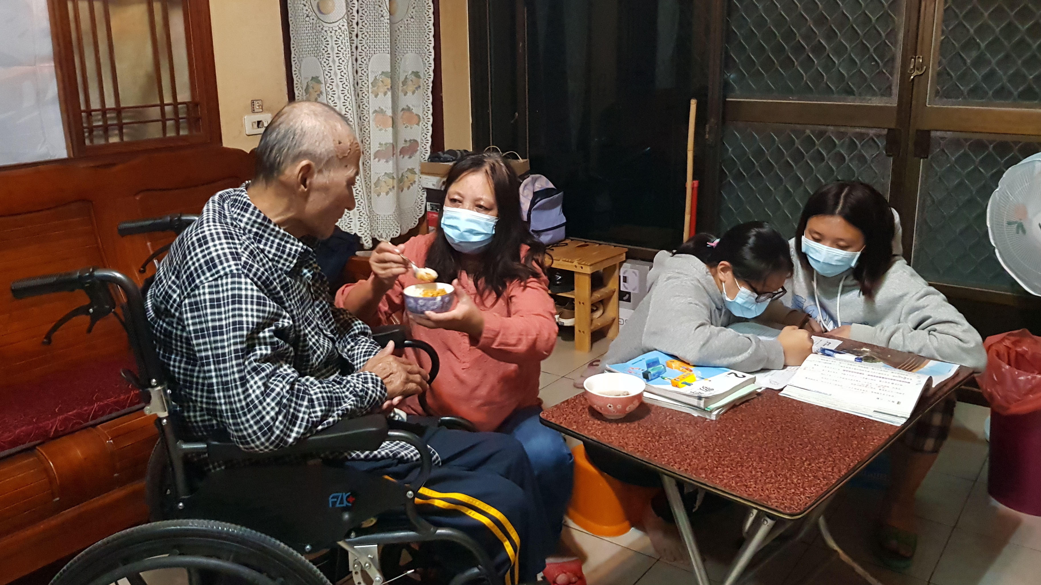 阿妹婆(左2)照料中風的老伴阿權伯(左1)吃飯,外孫女小韻(右1)、小盈在一旁做功課。韓旭爾攝 阿妹婆(左2)照料中風的老伴阿權伯(左1)吃飯,外孫女小韻(右1)、小盈在一旁做功課。韓旭爾攝