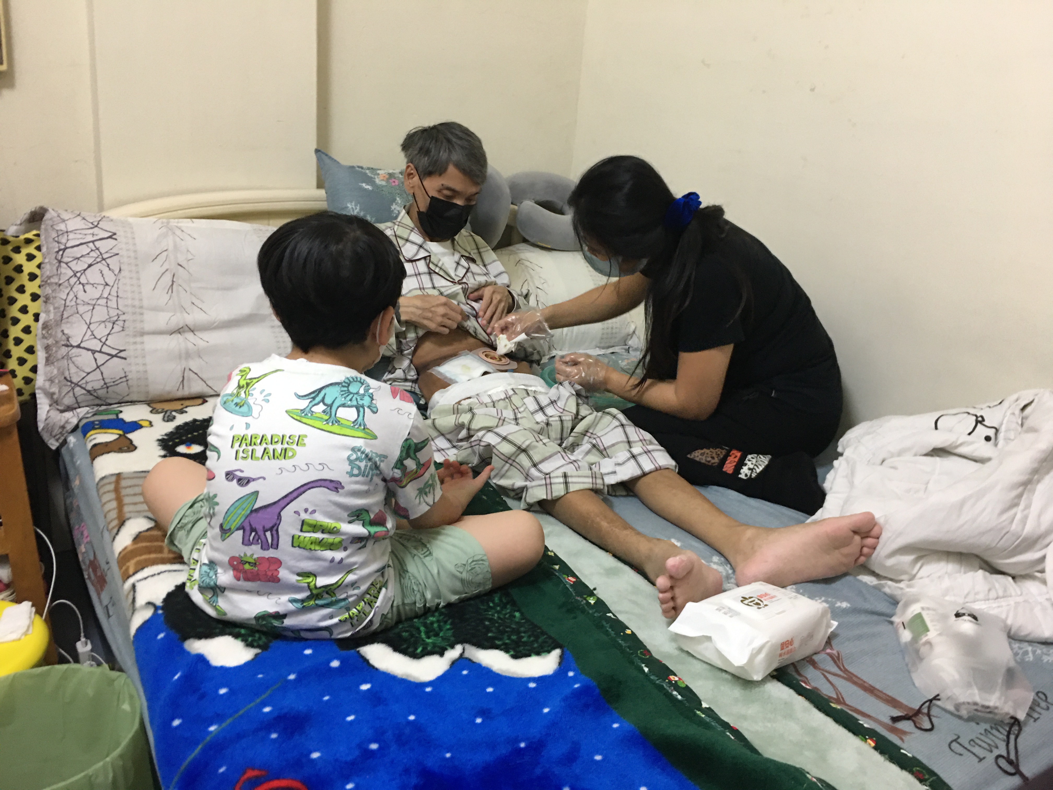 江民誌(中)罹癌病重,太太阿佳(右)在旁照顧。向高彬攝 江民誌(中)罹癌病重,太太阿佳(右)在旁照顧。向高彬攝
