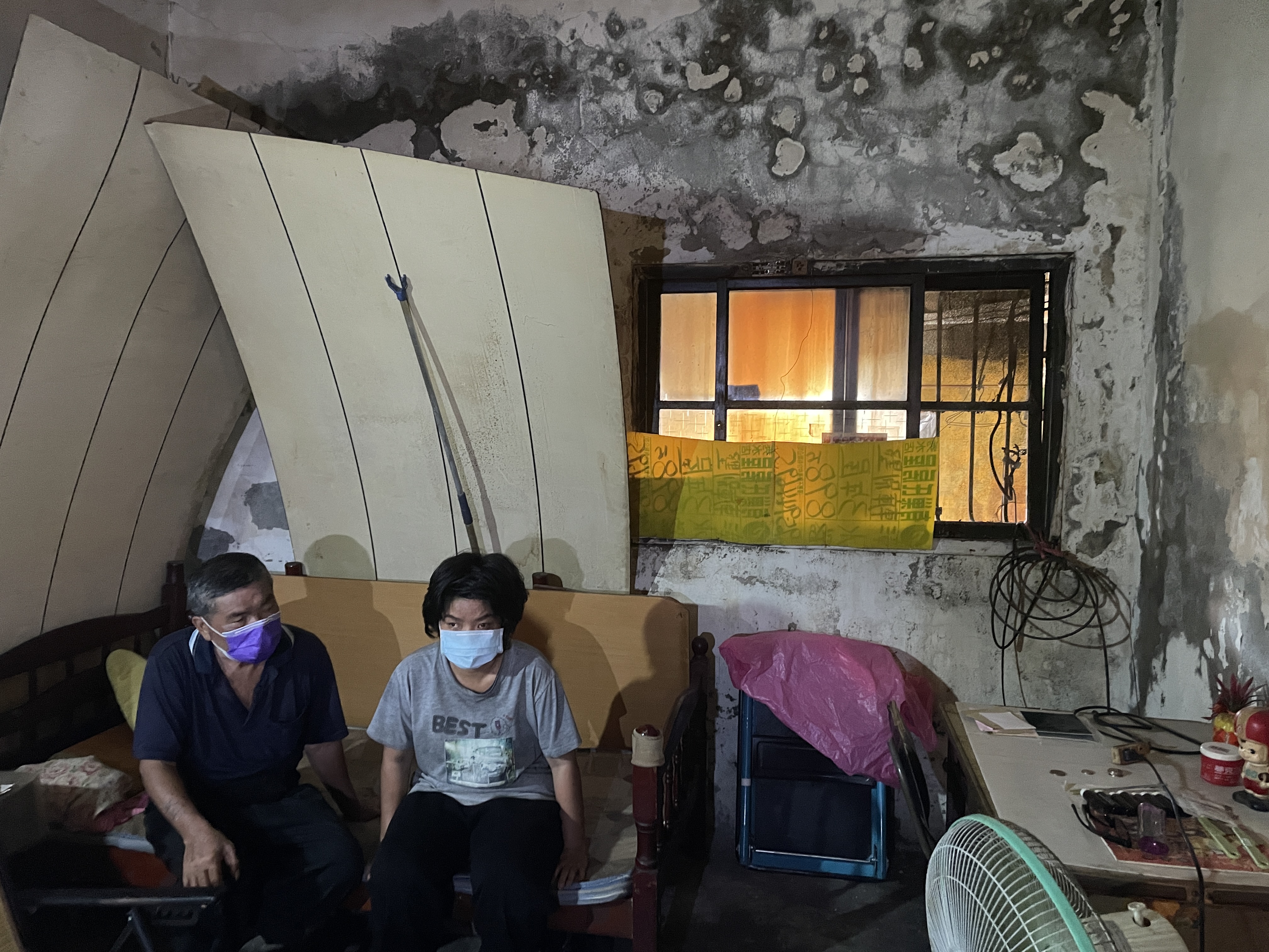 陳義廉(左)與28歲智能障礙女兒小秀(右)因租屋處漏水嚴重,陳義廉睡客廳僅能用木板擋住漏水,避免滴到床上。李佳玲攝 陳義廉(左)與28歲智能障礙女兒小秀(右)因租屋處漏水嚴重,陳義廉睡客廳僅能用木板擋住漏水,避免滴到床上。李佳玲攝