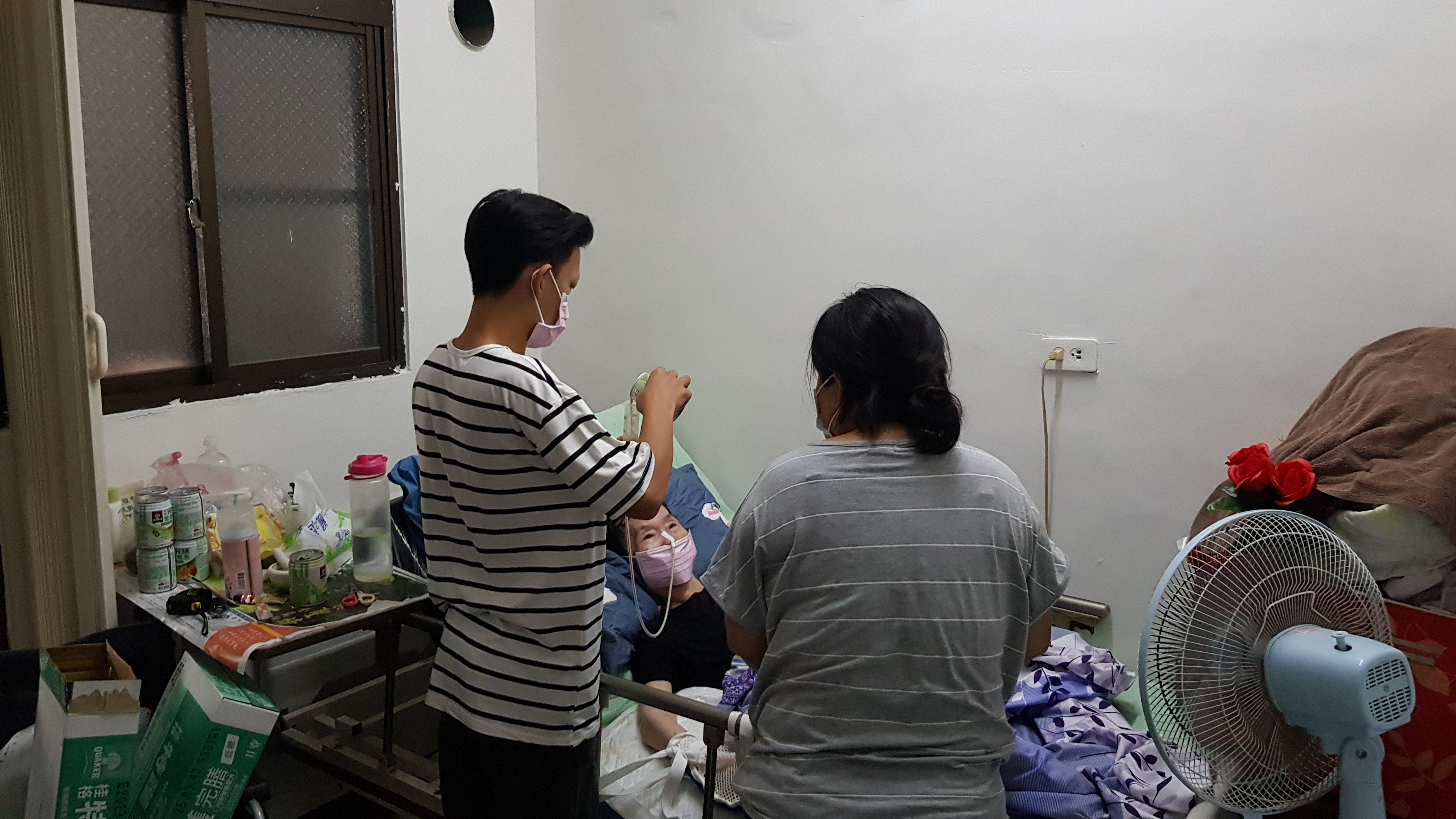 阿梅(前右)和次子小斌(前左)幫臥床的婆婆管灌營養品。韓旭爾攝 阿梅(前右)和次子小斌(前左)幫臥床的婆婆管灌營養品。韓旭爾攝